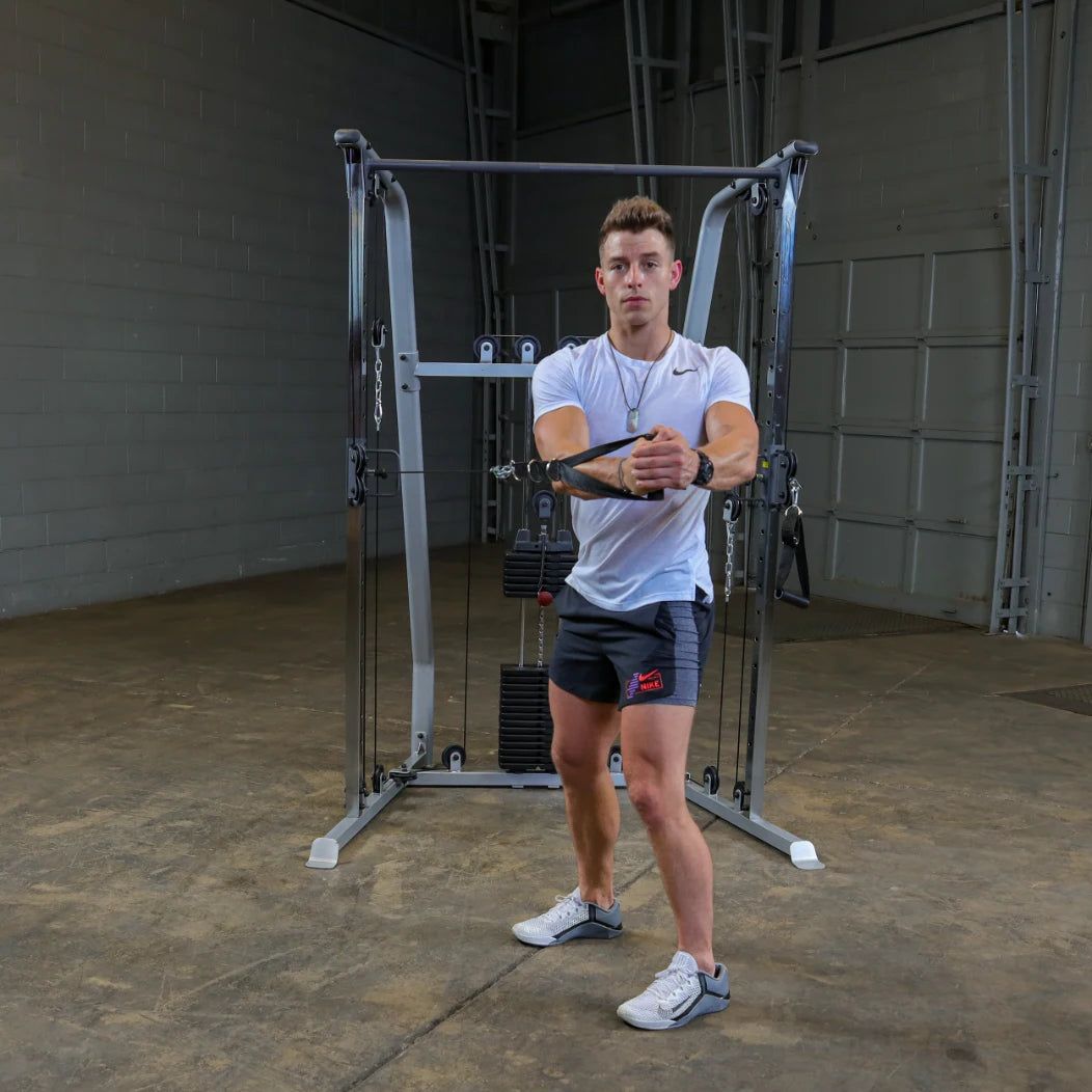 A young man in a white t-shirt and black shorts performs a cable exercise with a fitness machine in a gym setting.