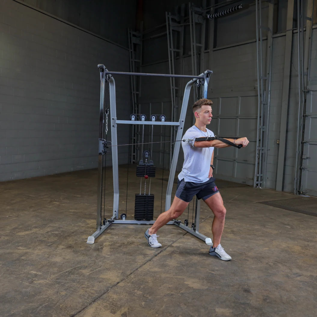 A young man in athletic wear performs a cable exercise in a gym setting, using a cable machine with weights. He is extending one arm forward while maintaining a stable stance.