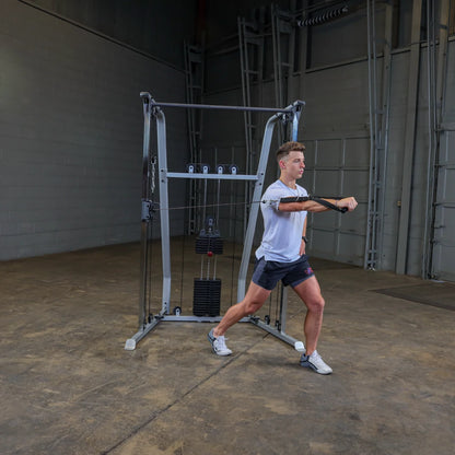 A young man in athletic wear performs a cable exercise in a gym setting, using a cable machine with weights. He is extending one arm forward while maintaining a stable stance.