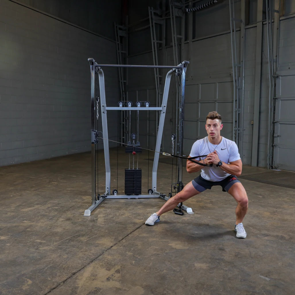 A person performing a resistance training exercise using a cable machine in a gym setting. The individual is in a squat position, holding the cable with both hands, and appears focused on their workout.