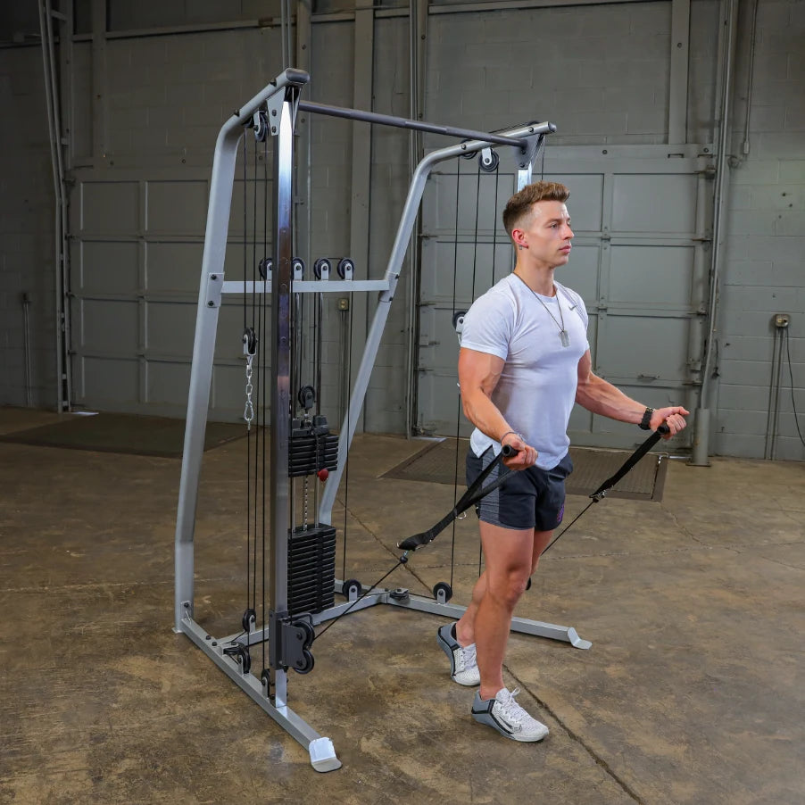 A young man in a white t-shirt and shorts performing a cable exercise using a cable machine in a gym setting.