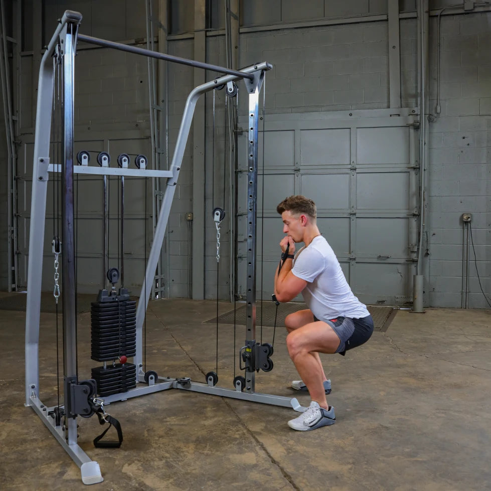 A person performing a squat exercise using a cable machine in a gym setting, with weights attached to the machine.