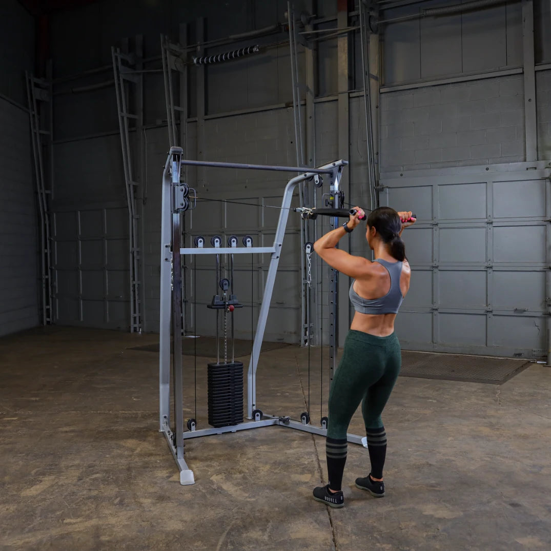 A woman with a strong physique is performing an exercise on a cable machine in a gym setting, demonstrating strength training.