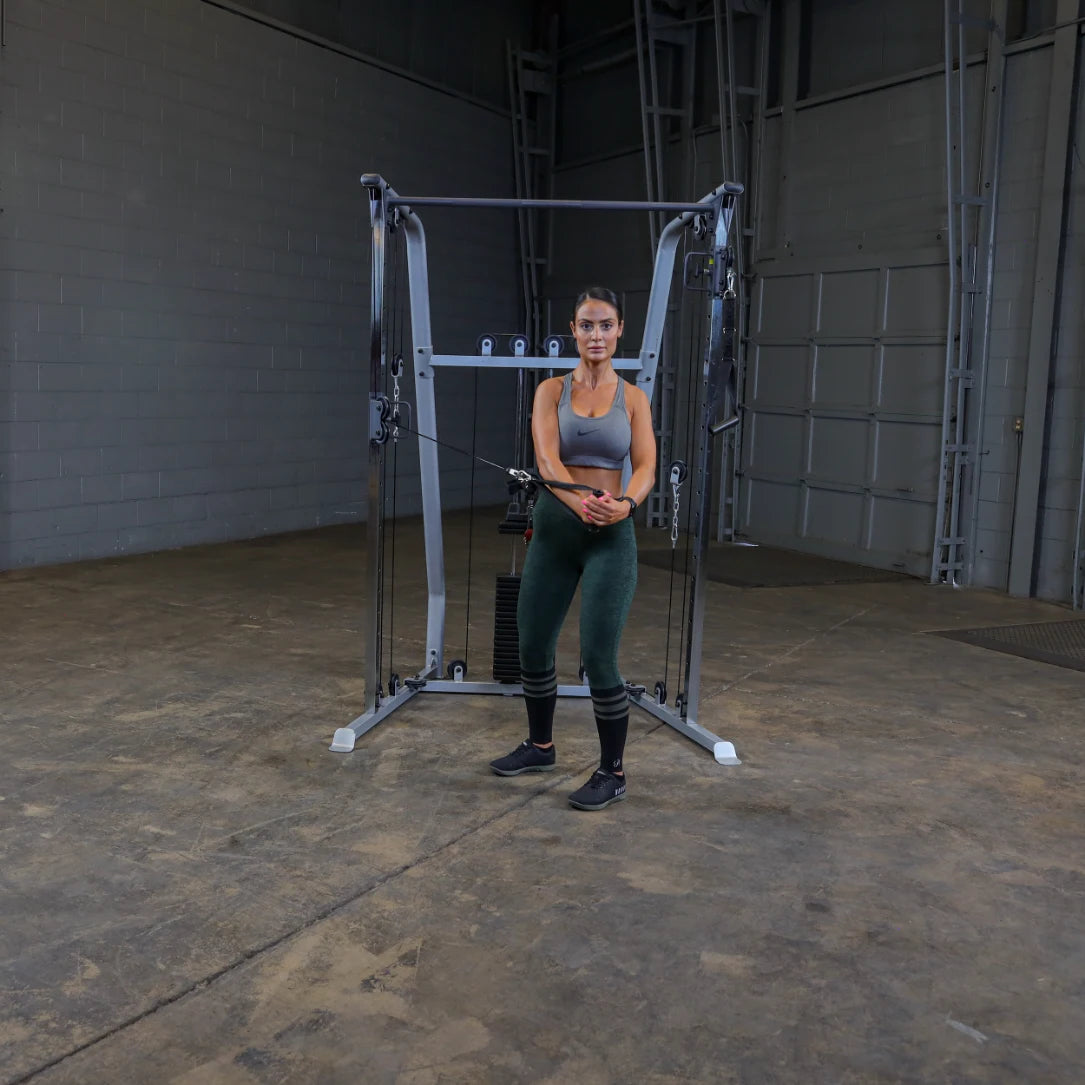 A woman in athletic wear stands in front of a cable machine in a gym setting, preparing to perform an exercise.