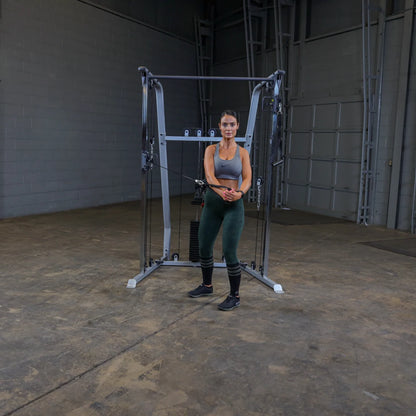 A woman in athletic wear stands in front of a cable machine in a gym setting, preparing to perform an exercise.