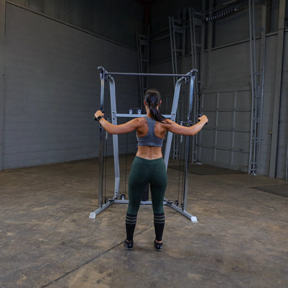 A person performing a workout on a cable machine in a gym setting, wearing a gray sports bra and green leggings, with their back facing the camera.