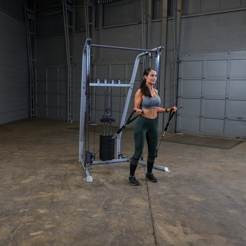 A woman in athletic wear performs a strength training exercise with resistance bands attached to a cable machine in a spacious gym setting.