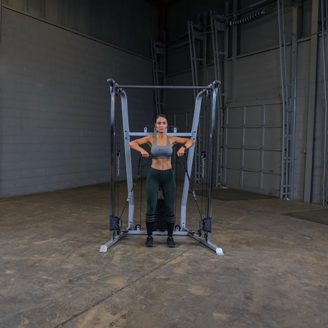 A woman in athletic wear performs an exercise using a cable machine in a gym setting, demonstrating strength training with her arms extended.