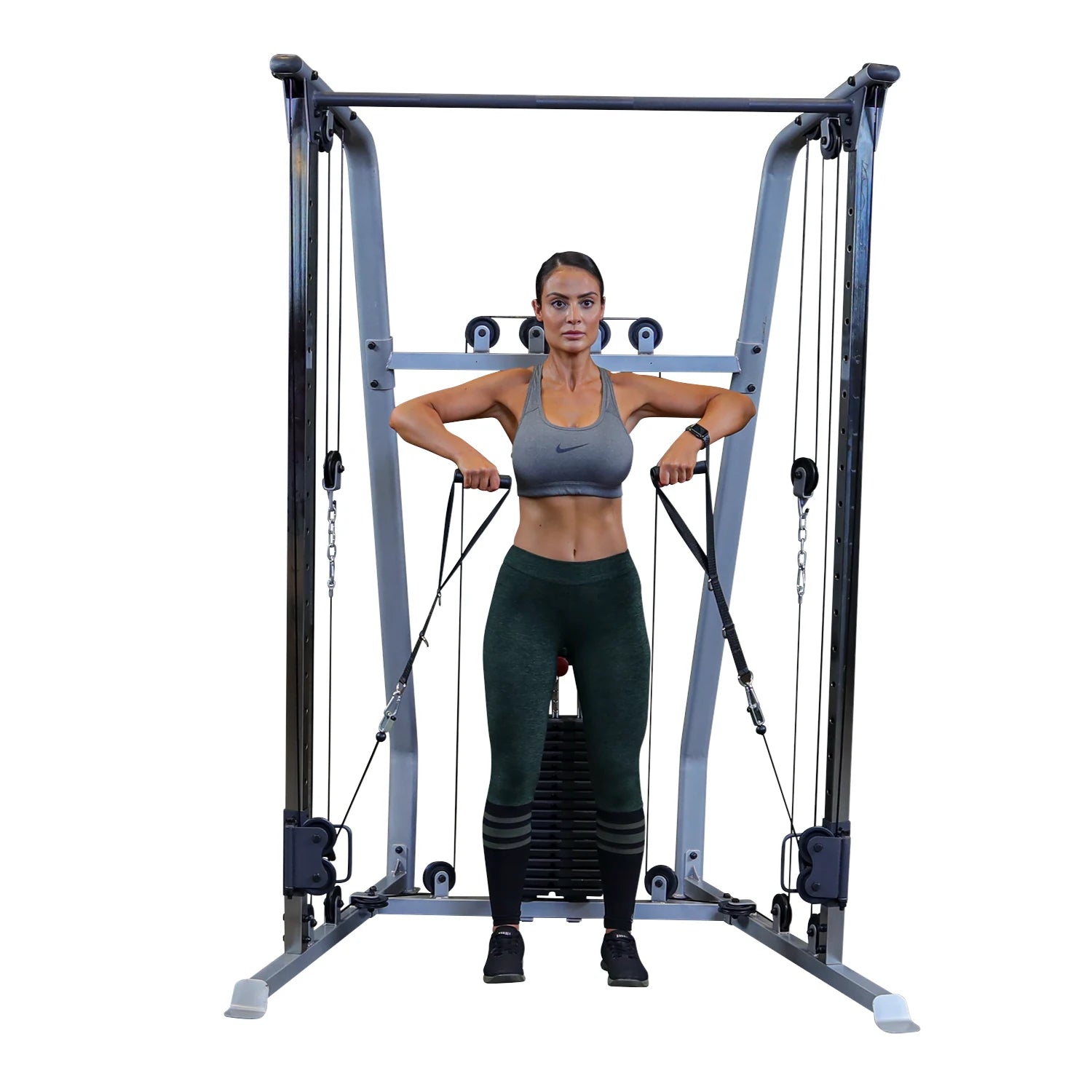 A woman in athletic wear performs a cable exercise using a gym machine, focusing on strength training. She has a serious expression and is holding the cables with both hands, positioned in front of her body.