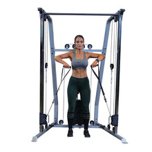 A woman in athletic wear performs a cable exercise using a gym machine, focusing on strength training. She has a serious expression and is holding the cables with both hands, positioned in front of her body.