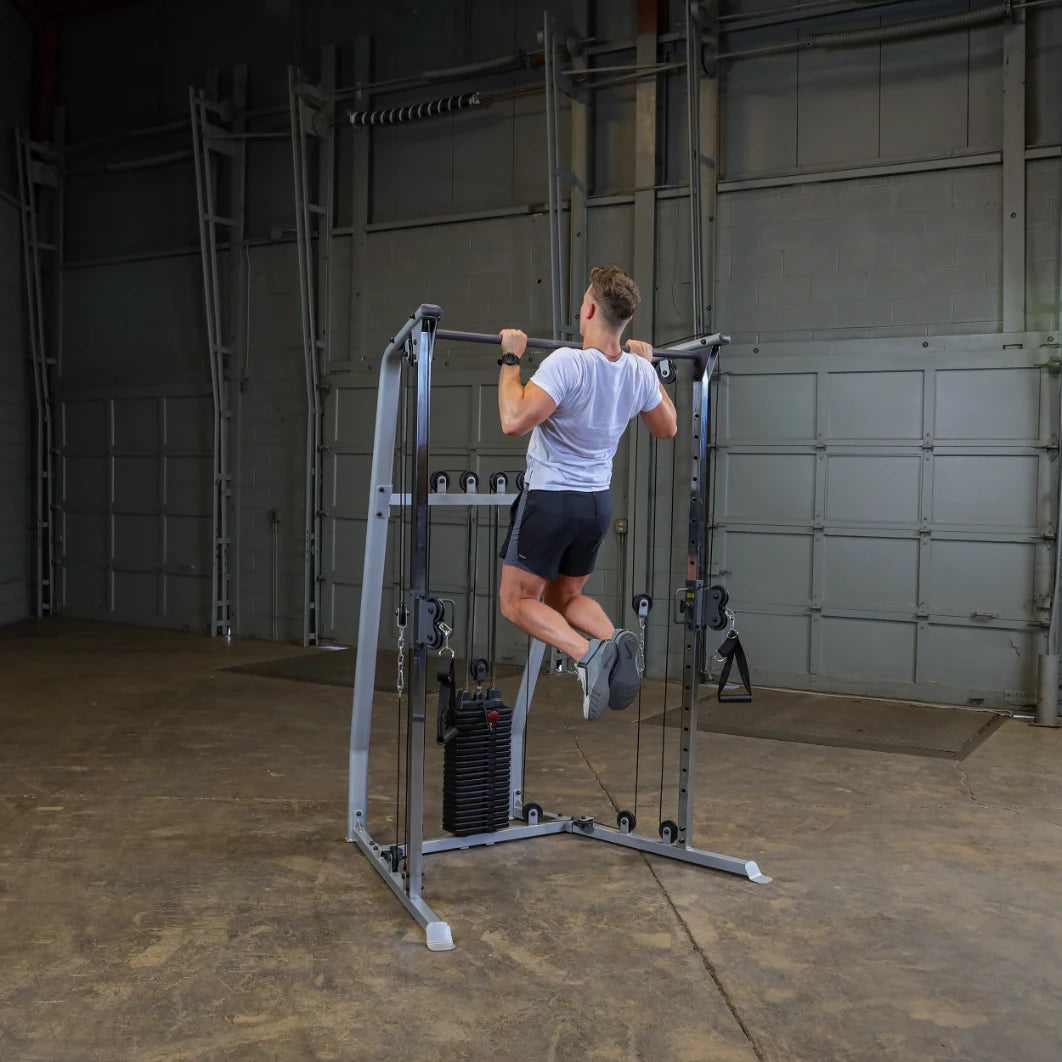 A person performing a pull-up on a gym machine in a spacious workout area with concrete flooring and a garage-style background.