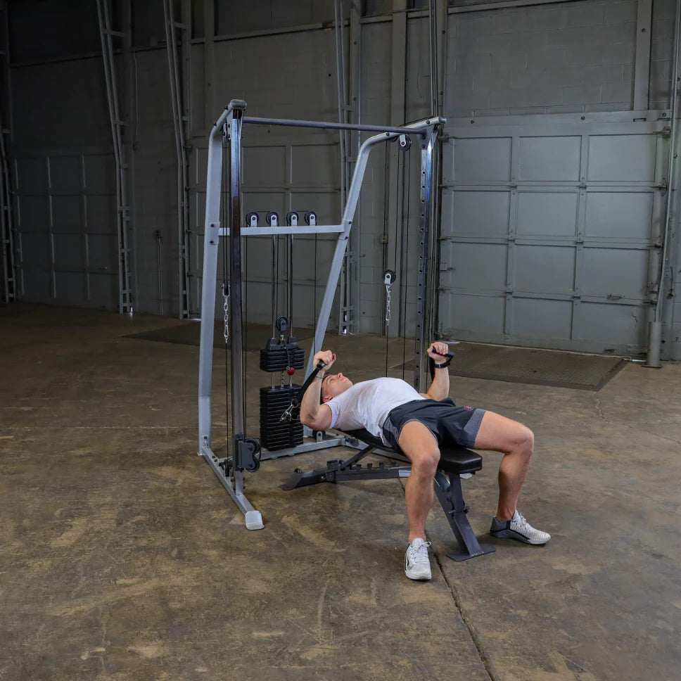 A person exercising on a cable machine in a gym setting, performing a workout while lying on a bench, with weights visible on the machine.
