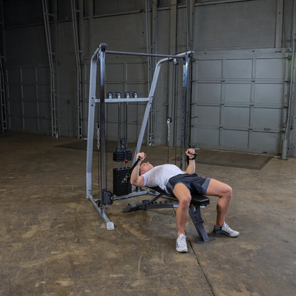 A person exercising on a cable machine in a gym setting, performing a workout while lying on a bench, with weights visible on the machine.
