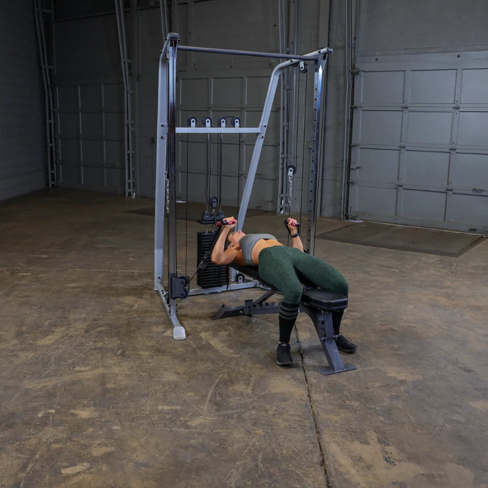 A person exercising on a cable machine in a gym setting, performing a workout while lying on a bench, wearing athletic clothing.