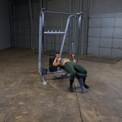 A person exercising on a cable machine in a gym setting, performing a workout while lying on a bench, wearing athletic clothing.