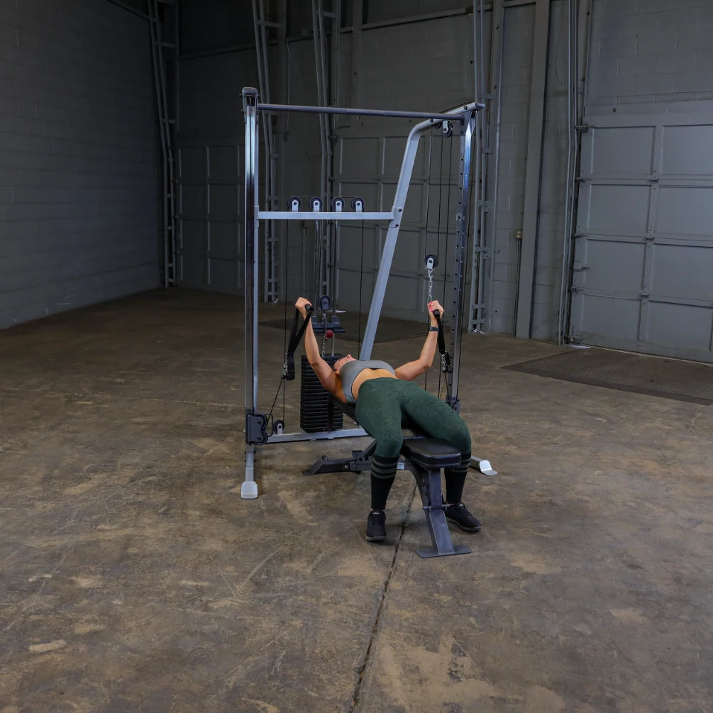Person exercising on a cable machine in a spacious gym, performing a workout while lying on a bench, wearing athletic clothing.
