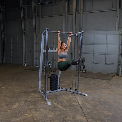 A person performing an exercise on a cable machine, hanging from the overhead bar with legs raised in a gym setting.