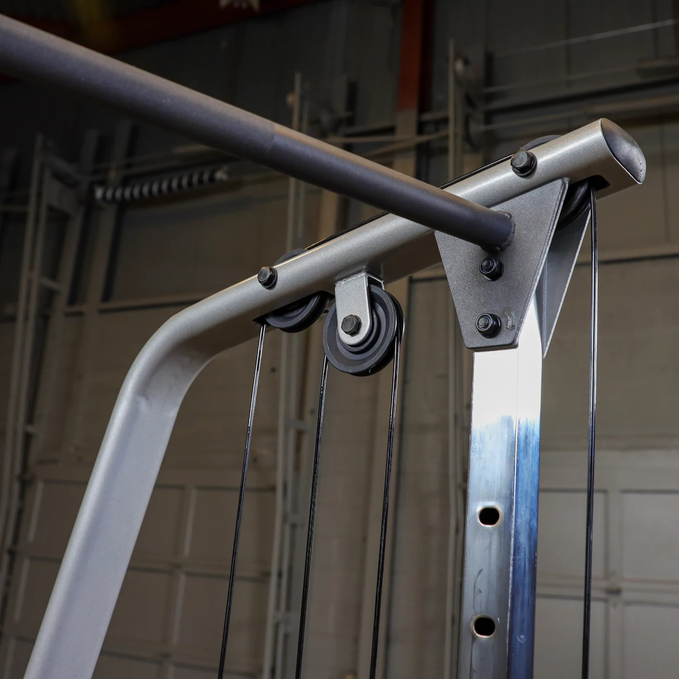 Close-up of a gym cable machine showing the pulley system, cables, and metal frame, with a focus on the adjustable bar and components in a fitness environment.