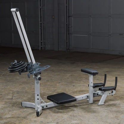 A silver and black multi-functional gym machine with a weight plate attached, set against a concrete floor and a garage door background.
