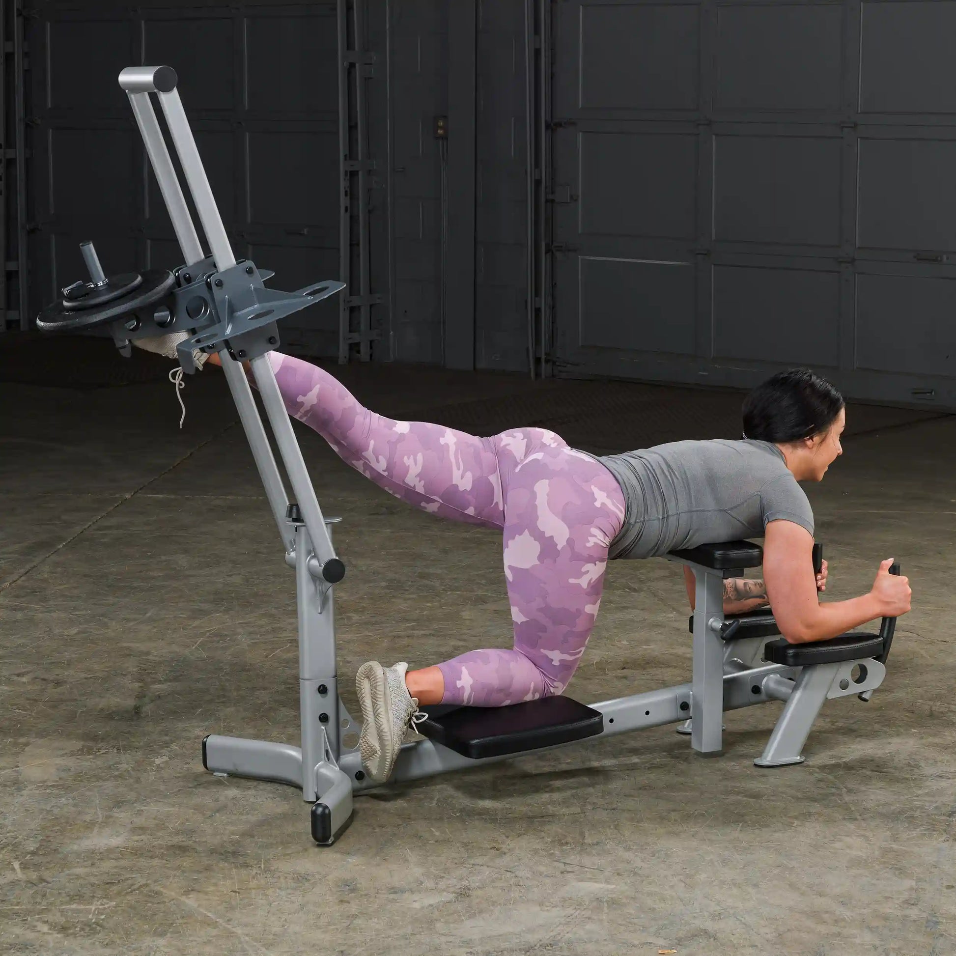 A person performing an exercise on a gym machine, focusing on their legs, wearing a gray shirt and pink camo leggings.
