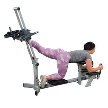 A woman performing an exercise on a gym machine, focusing on her leg workout. She is wearing gray athletic wear and pink camo leggings, demonstrating proper form with her left leg extended on the machine.