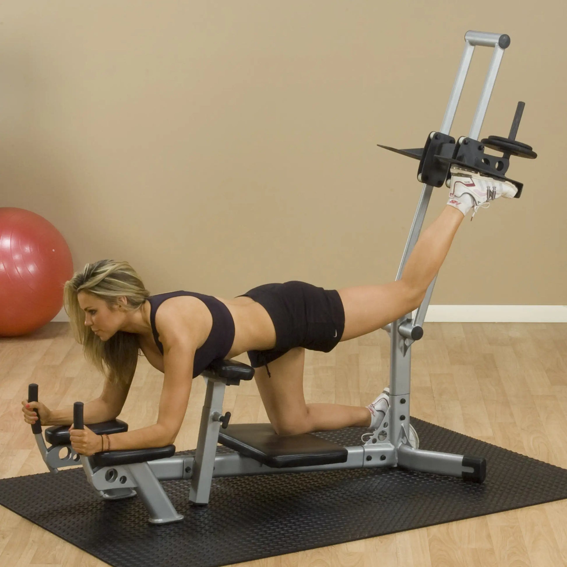 A woman performing a leg workout on a gym machine, focusing on her form and posture, with a stability ball in the background.