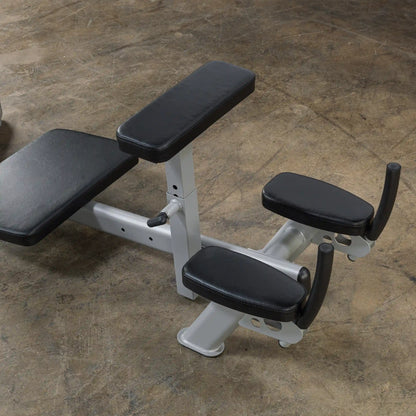 A close-up view of a weightlifting bench with two padded arm supports and a black and silver design, placed on a textured floor.
