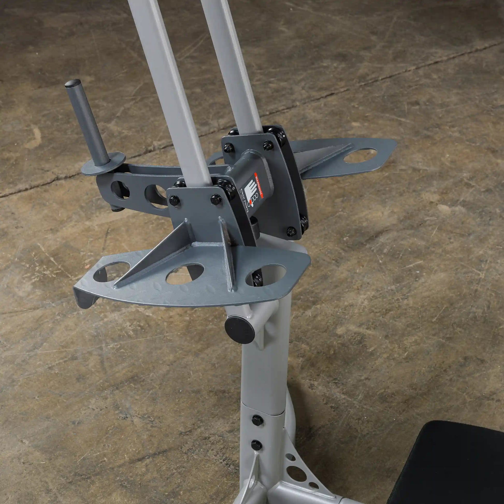 Close-up view of a weightlifting machine's adjustable arm and support structure, featuring a gray metallic finish, set against a textured concrete floor.