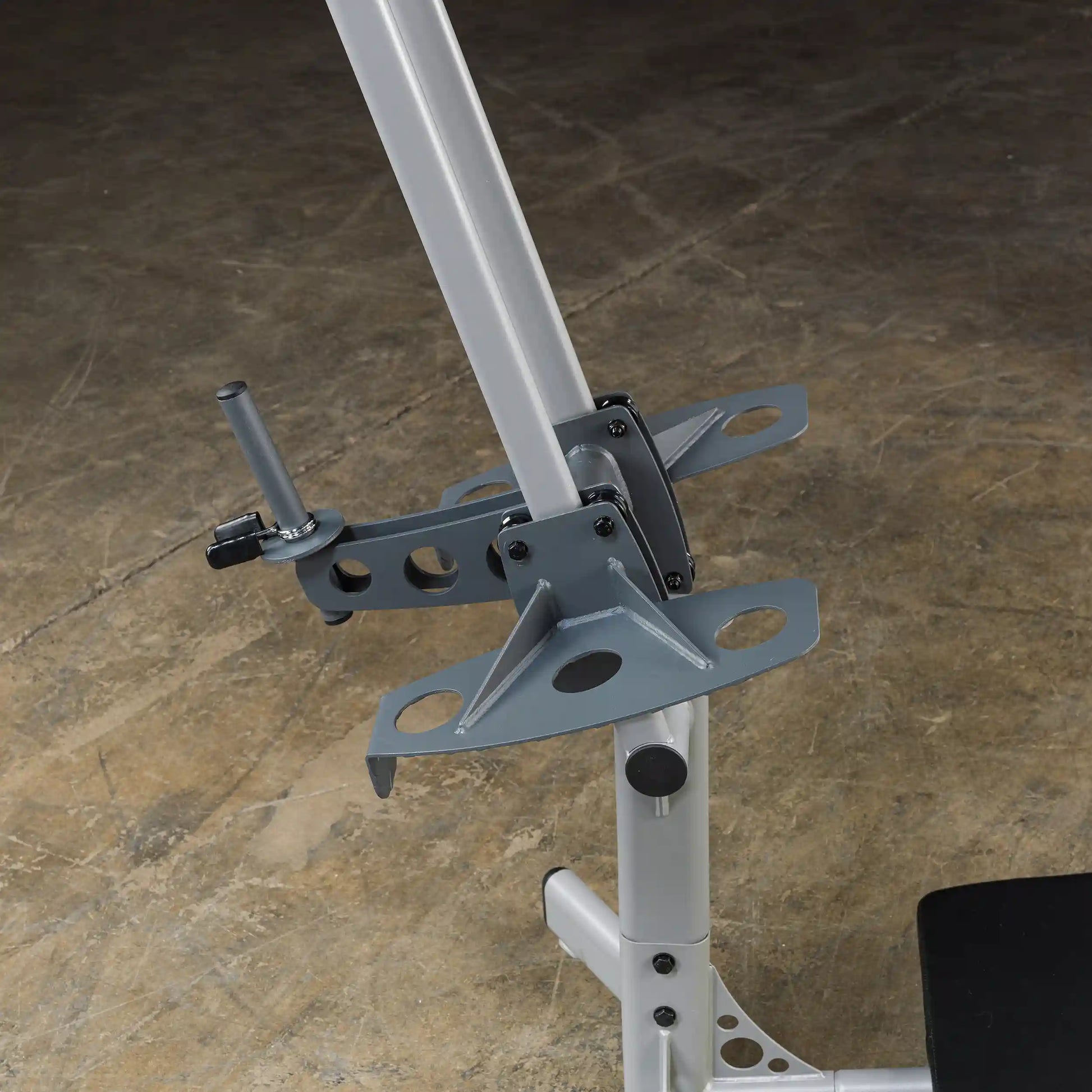 Close-up view of a gray metal bracket attached to a vertical pole, featuring a locking mechanism and multiple holes for adjustments, set against a textured floor surface.