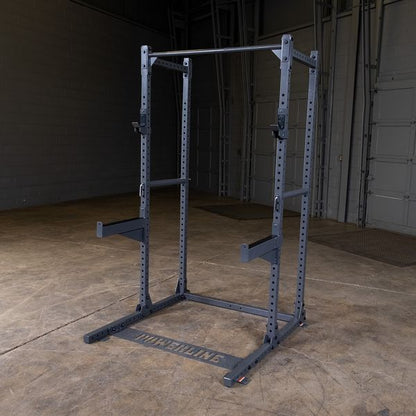 A sturdy black squat rack positioned on a concrete floor in a gym setting, with a simple backdrop of gray walls and doors.