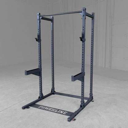 A black Powerline squat rack with adjustable pull-up bar and safety arms, set against a gray background in a gym or workout space.