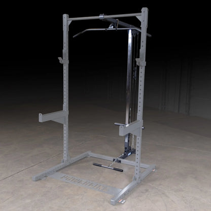 A gray weightlifting machine with a pull-up bar and adjustable cable system, set against a dark background on a concrete floor.