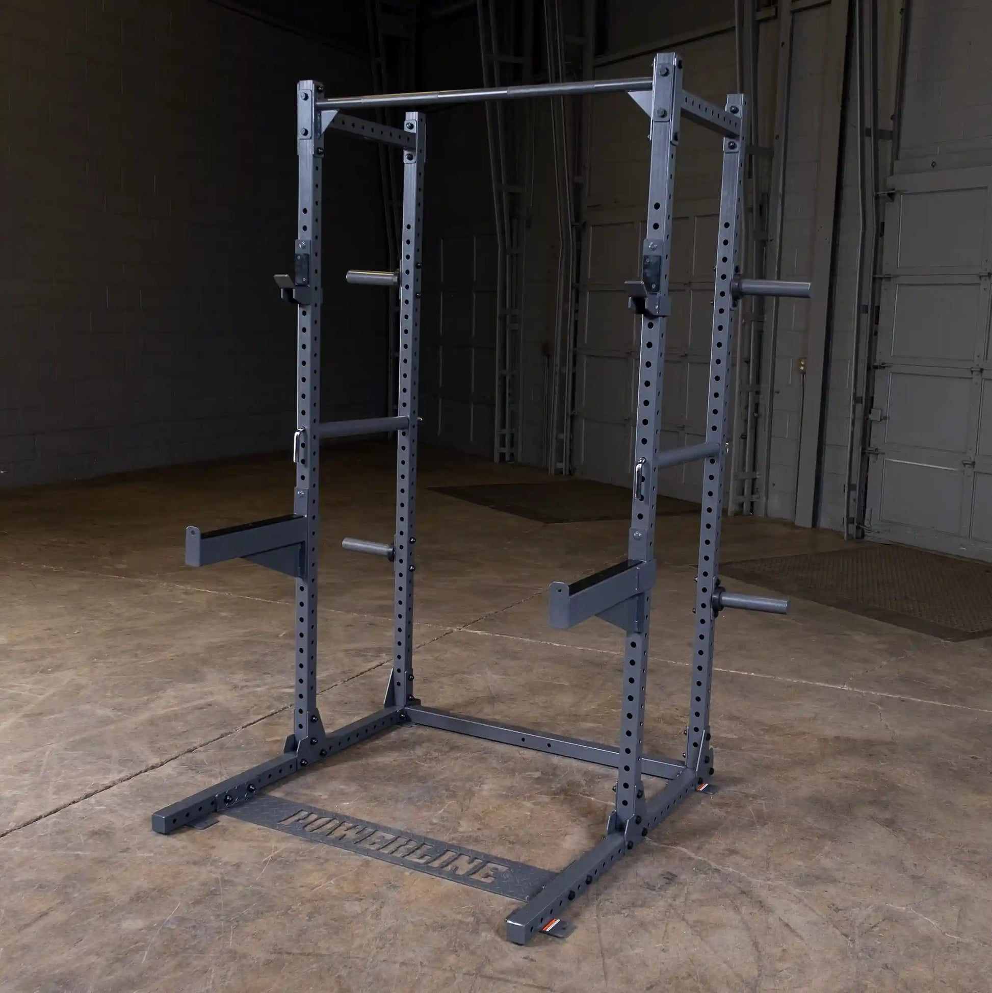 A black power rack for weightlifting, featuring adjustable bars and a sturdy frame, set against a concrete floor and walls in a gym-like environment.