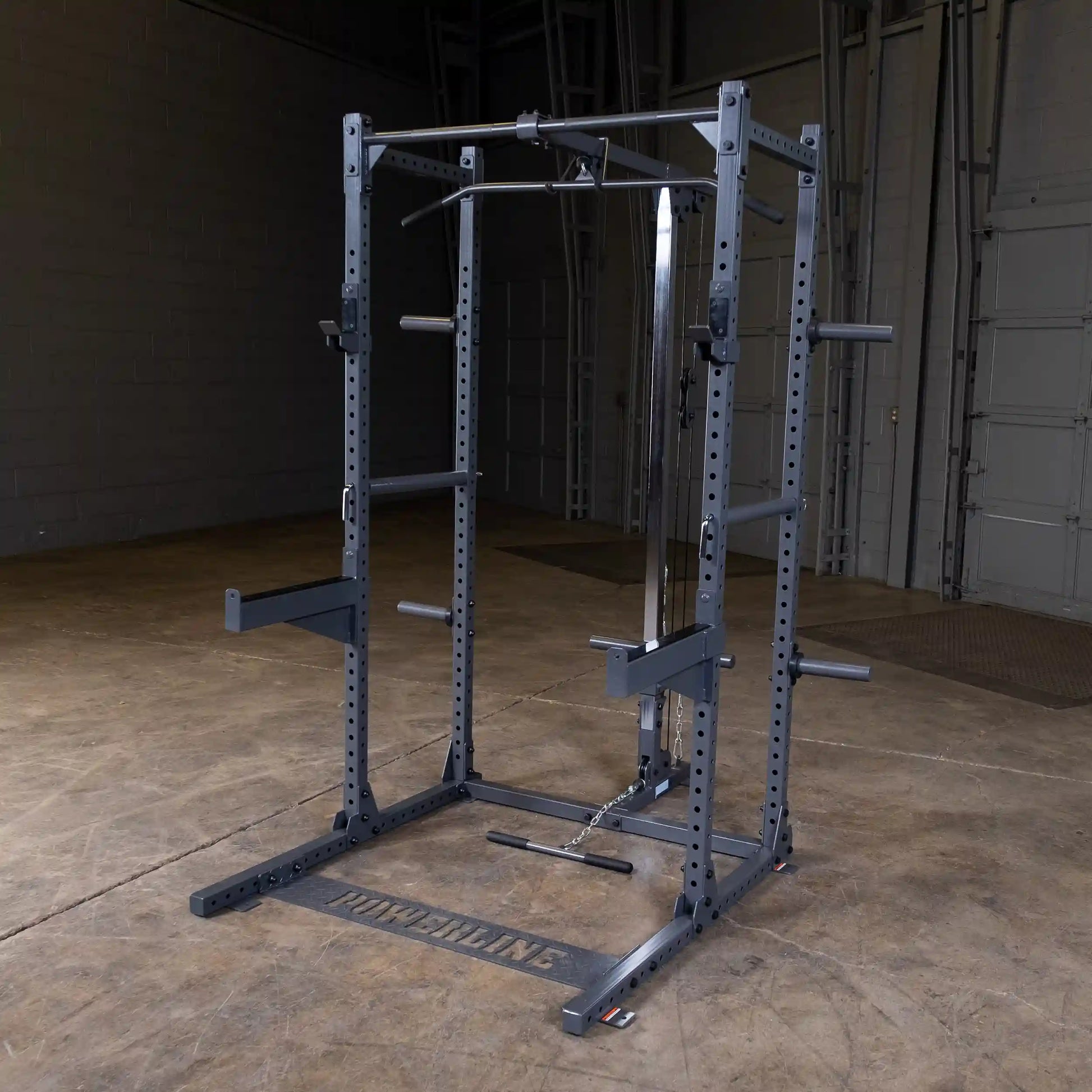 A power rack for strength training, featuring adjustable bars and a pull-up bar, set in a spacious gym environment with a wooden floor and gray walls.