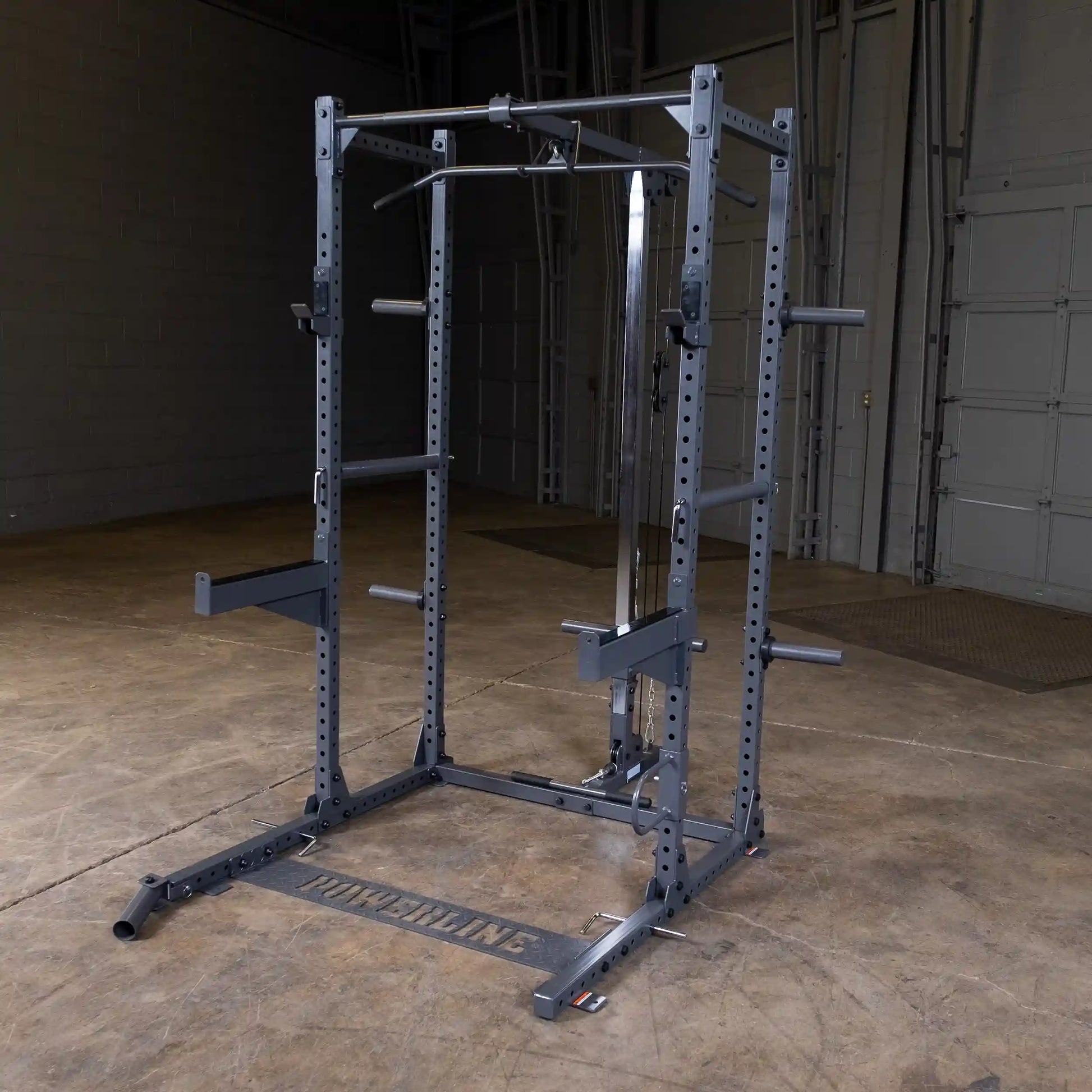 A gray power rack with multiple adjustable bars and attachments, set on a wooden floor in a gym-like environment.