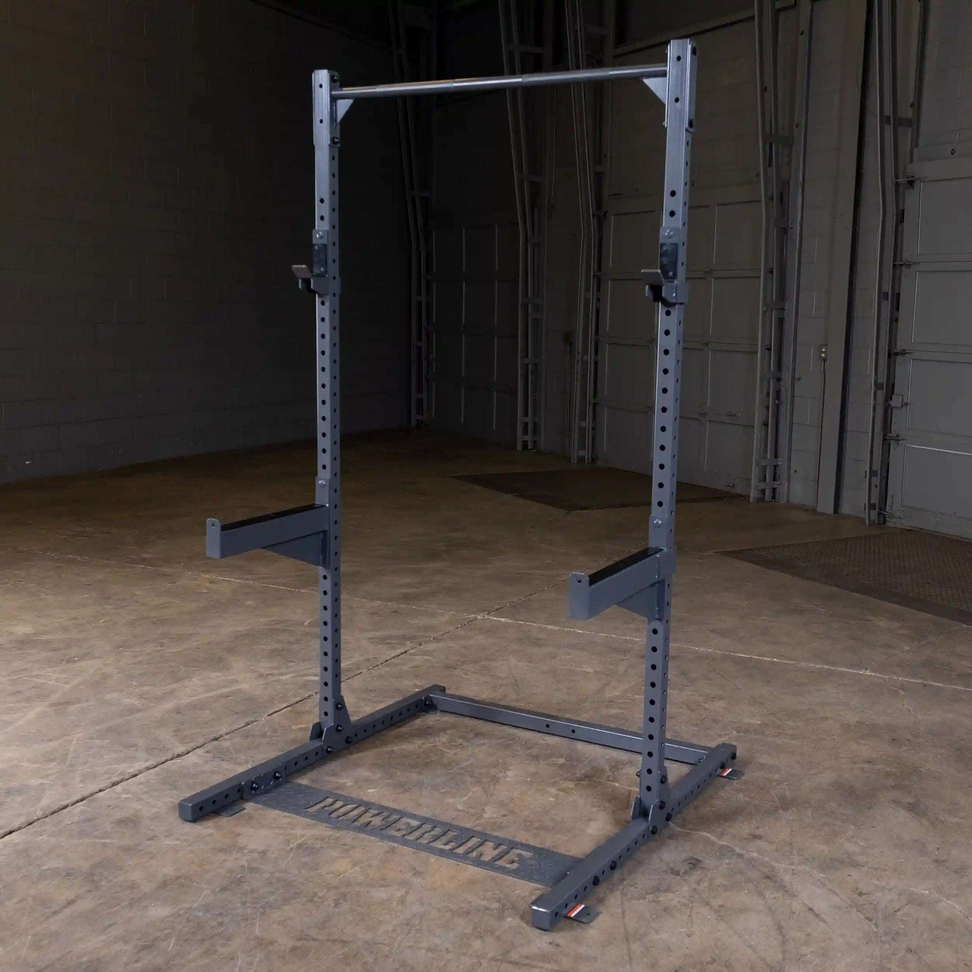 A power rack with a pull-up bar, designed for strength training, set on a concrete floor in a spacious indoor gym environment.