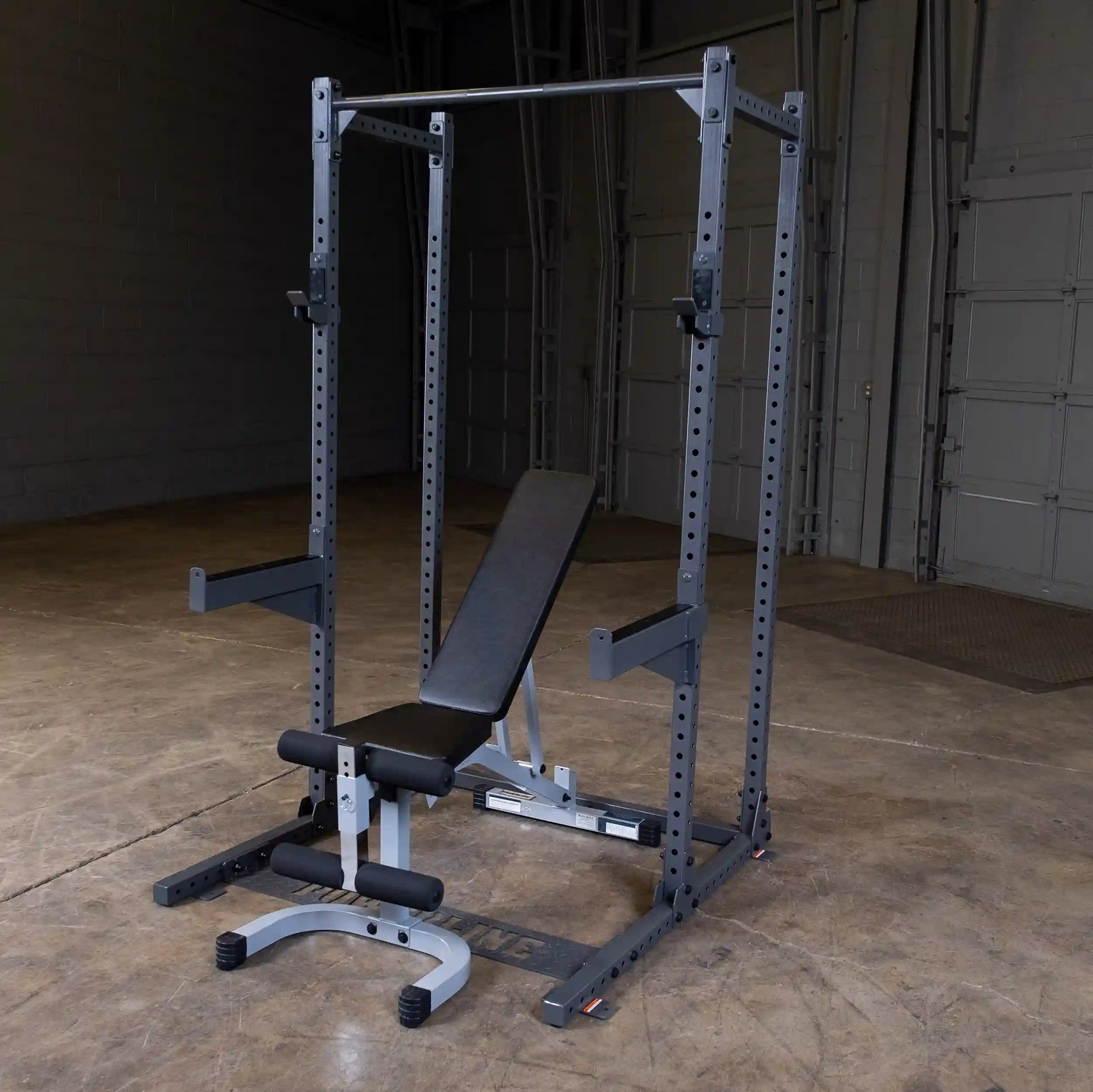 A black and silver weight bench with a squat rack in an empty gym setting, featuring a flat bench and adjustable bar supports.