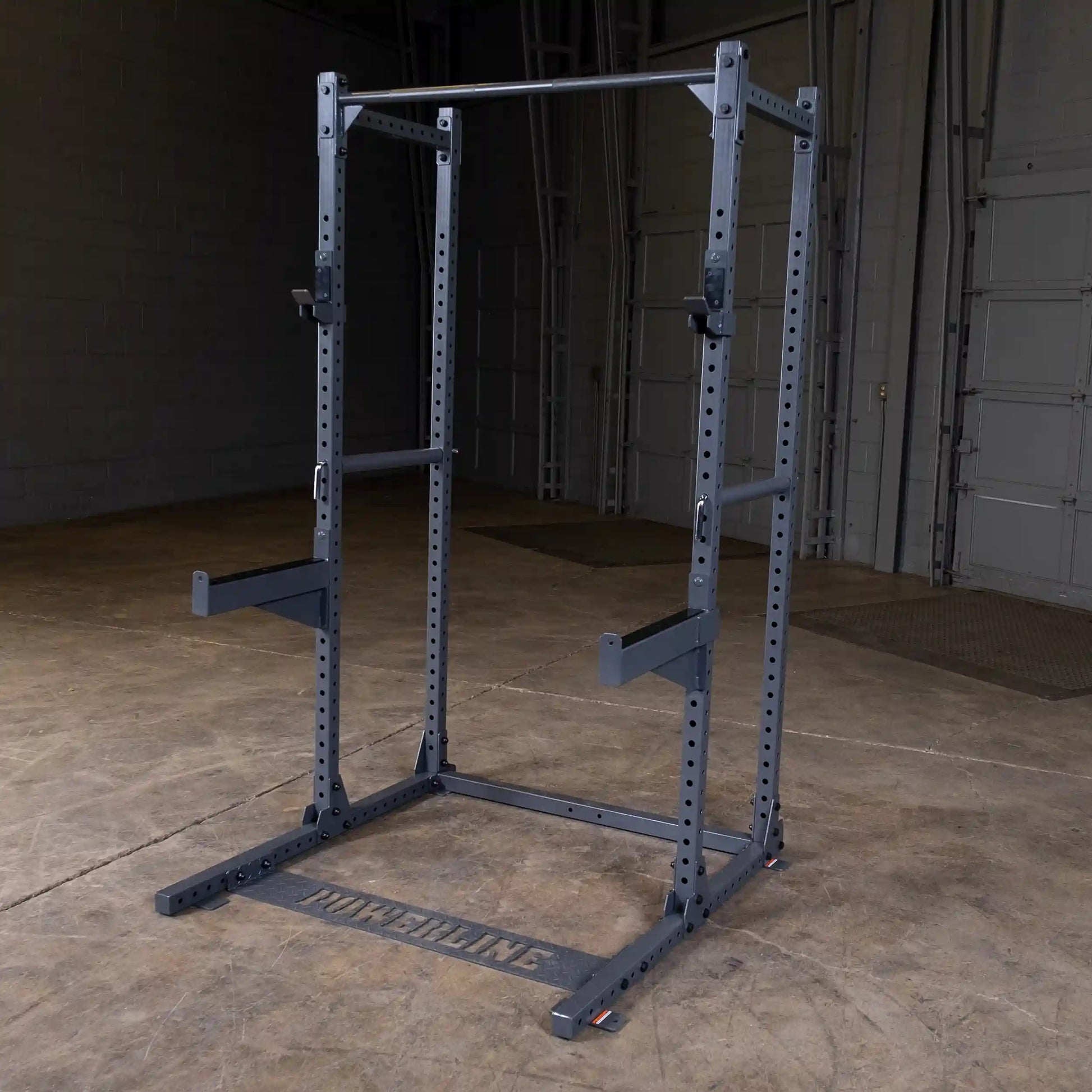 A heavy-duty squat rack made of metal, featuring adjustable height settings and a pull-up bar, set against a concrete floor in a spacious gym environment.