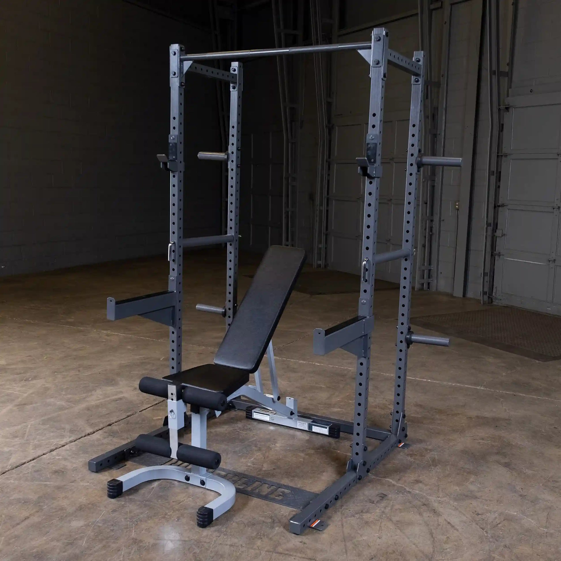 A weightlifting bench and squat rack set up in a spacious gym environment with a concrete floor and gray walls.