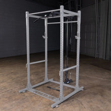 A gray Powerlifter rack with a pull-up bar and cable attachments, set in a large, empty gym space with a concrete floor.