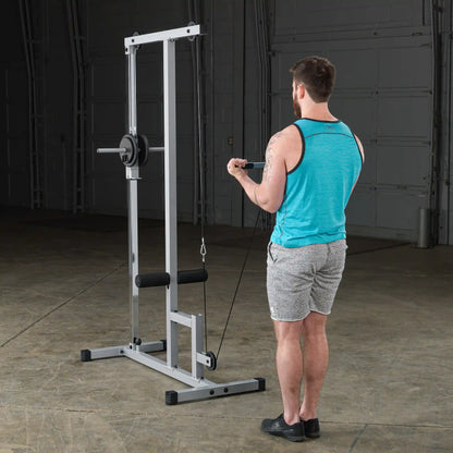 A man in a turquoise tank top and gray shorts performs a workout using a cable machine in a gym setting.