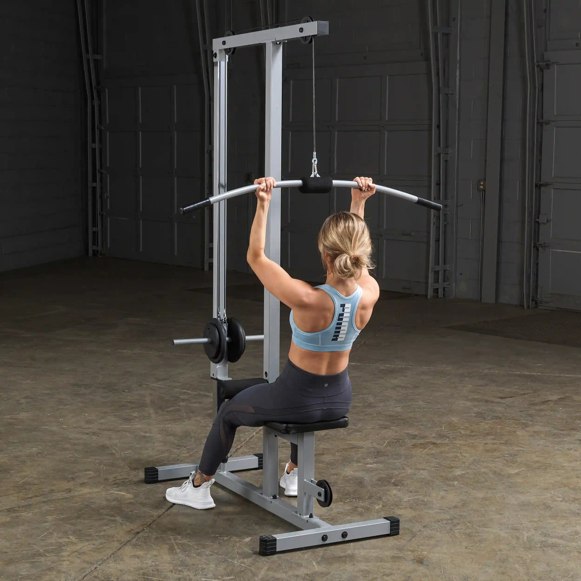A person performing a lat pulldown exercise on a cable machine in a gym setting, wearing a blue athletic top and black leggings, with a focus on their back and arms.