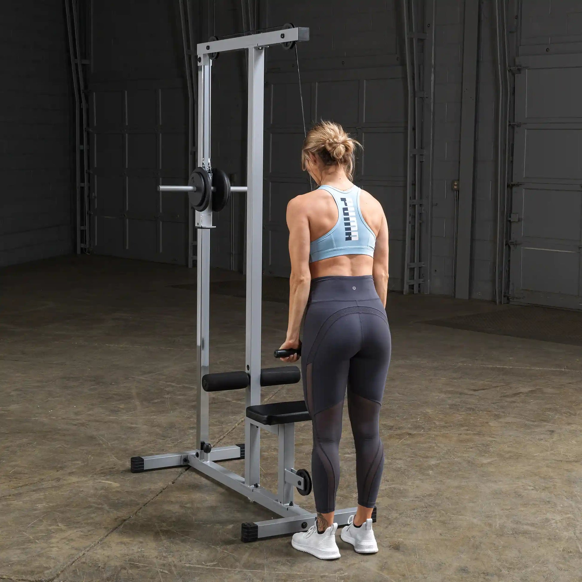 A woman in a blue sports bra and black leggings performs a workout using a cable machine in a gym setting.