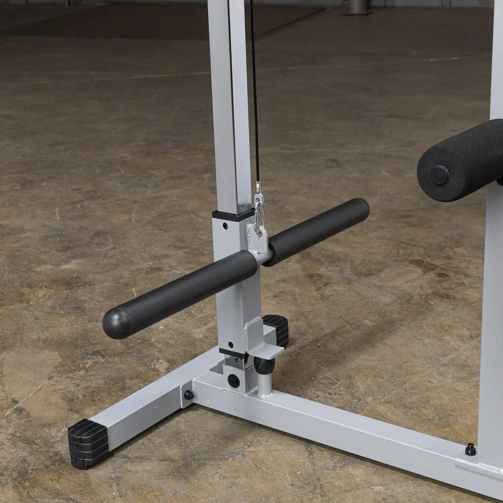 Close-up view of a weight training machine featuring a black padded handle and a cable system, set against a concrete floor background.
