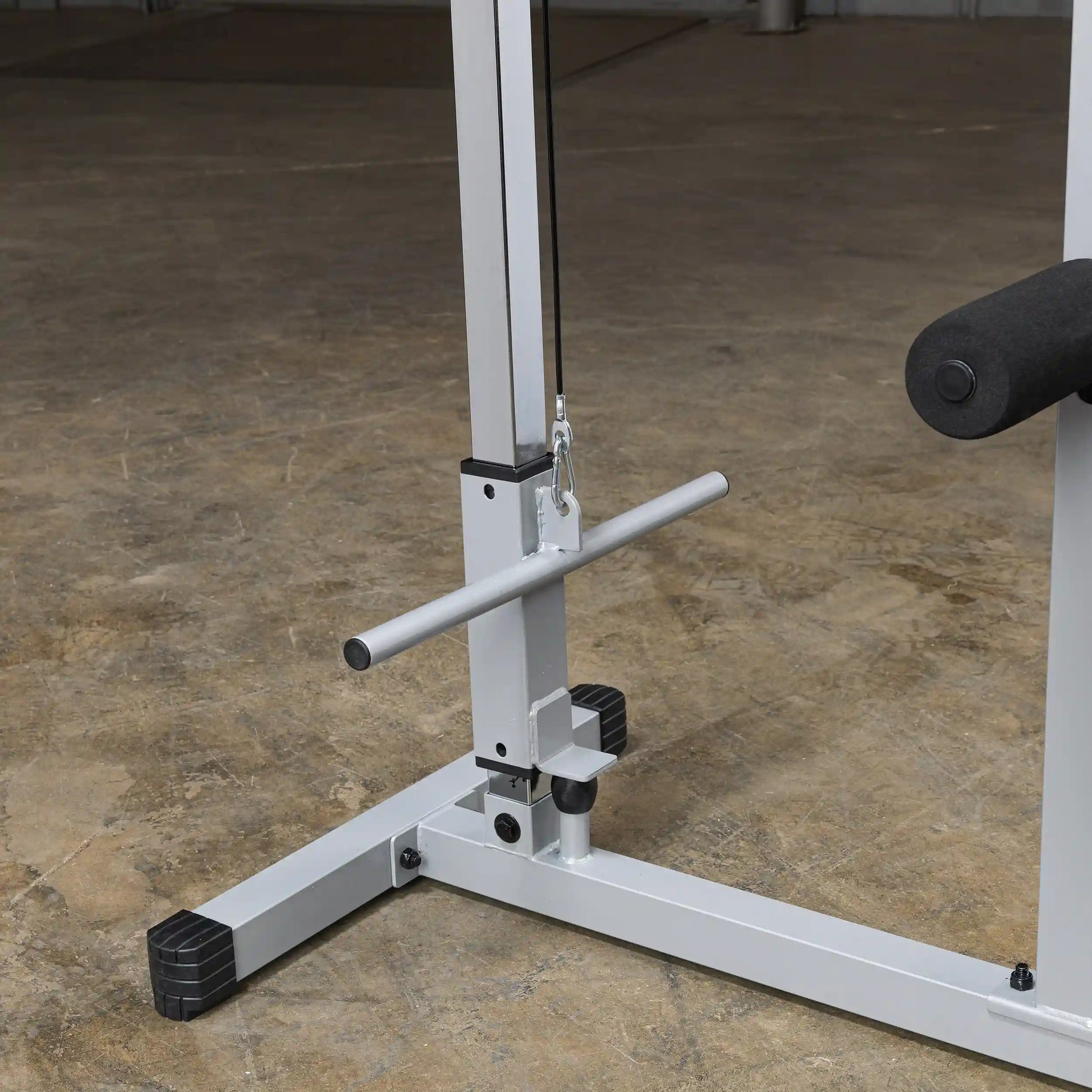 Close-up of a weight training machine's pulley system, featuring a horizontal bar and a padded support, set on a concrete floor.