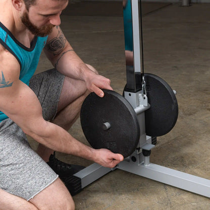 A person in a blue tank top and gray shorts is adjusting weights on a gym machine, focusing on the weight plates as they prepare for a workout.