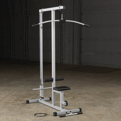 A silver cable machine for strength training, featuring a curved bar attachment, a seat, and foam rollers, set against a dark background in a gym or workout space.