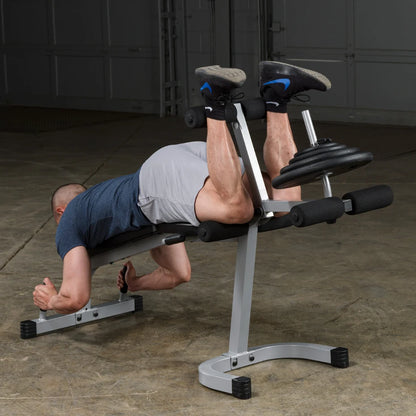 A person performing a back extension exercise on a fitness bench, with their legs elevated and a weight plate attached, in a gym setting.