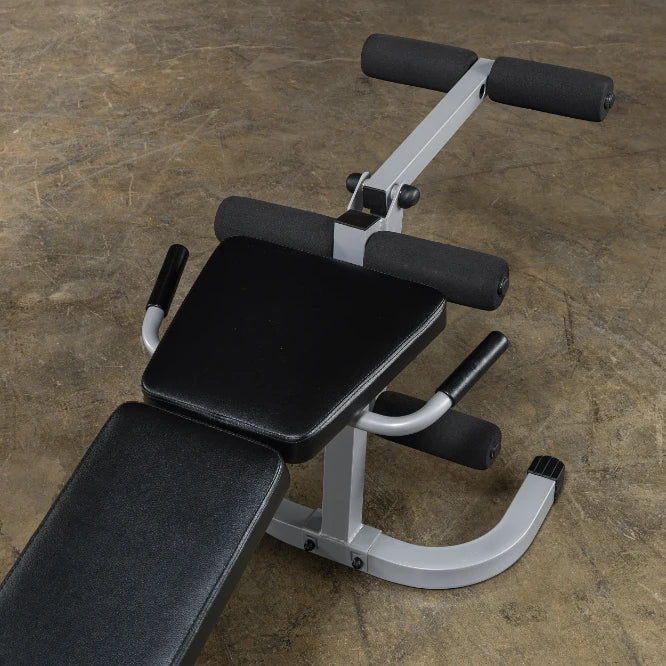 A close-up view of a black exercise bench with padded supports and handles, set against a textured concrete floor.