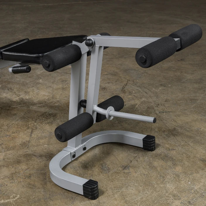 Close-up of a gym equipment piece featuring a padded seat and foam rollers, designed for abdominal workouts, resting on a concrete floor.
